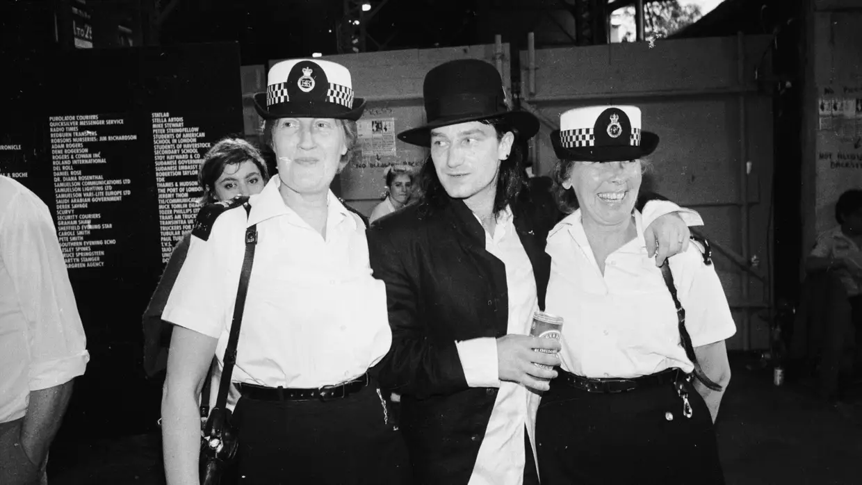 Bono rodeada de duas agentes da polícia nos bastidores do evento Live Aid, em 1985