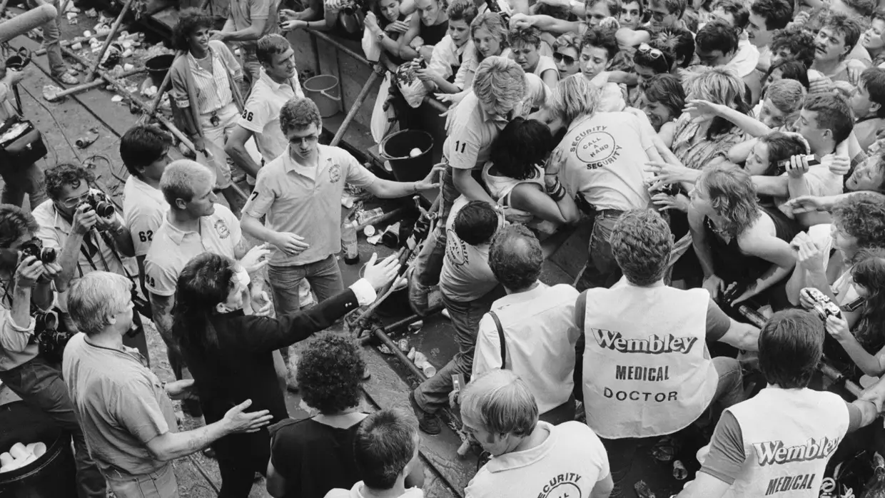 Bono vê os médicos a prestar assistência às filas da frente no espetáculo Live Aid, no Estádio de Wembley, em Londres, julho de 1985