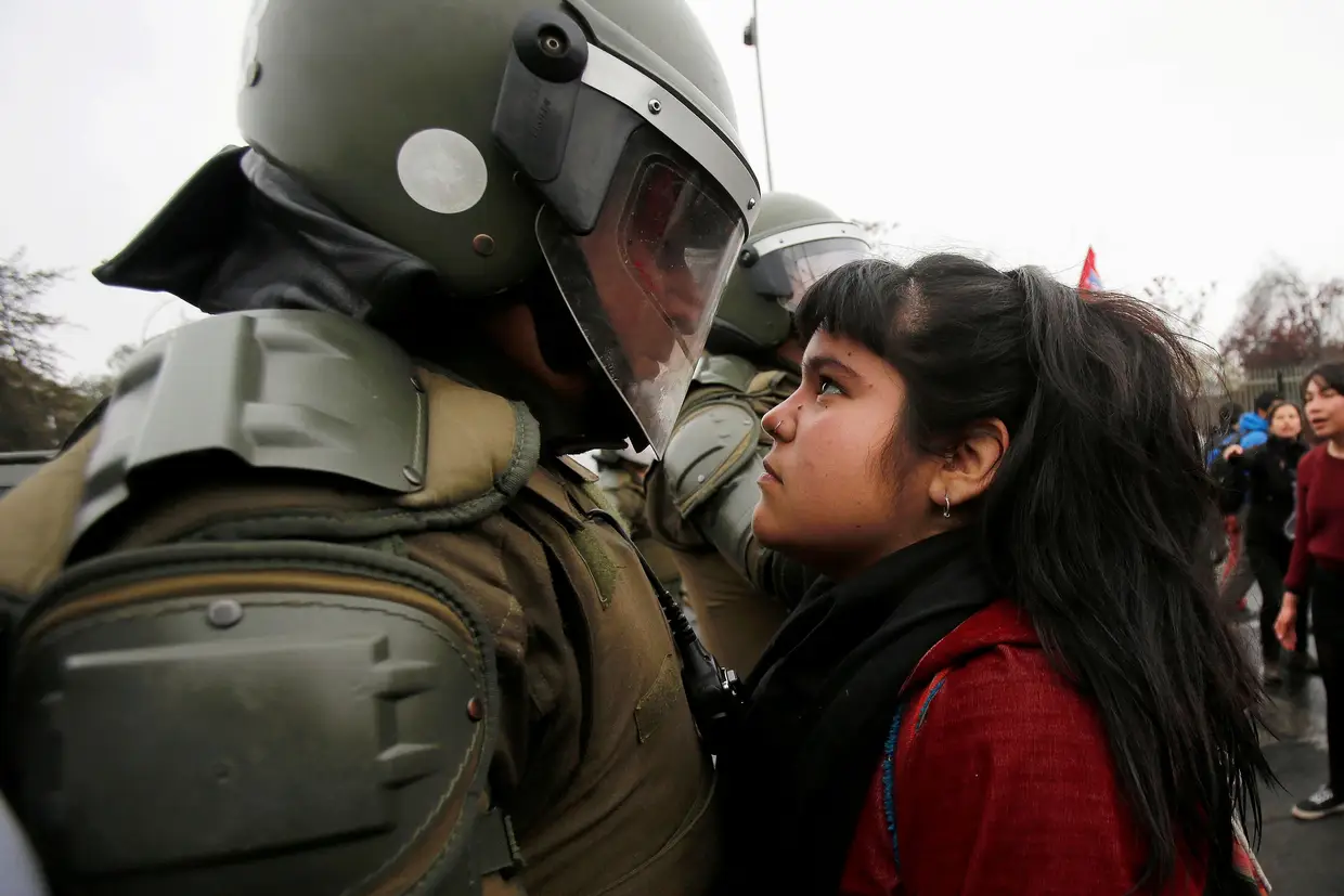 A troca de olhares entre uma manifestante e um agente da polícia de intervenção chilena, durante um protesto que assinalou o 43º aniversário do Golpe de Estado no país.