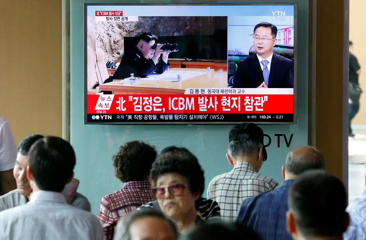 Várias pessoas concentram-se junto a um monitor numa estação ferroviária de Seul, Coreia do Sul,