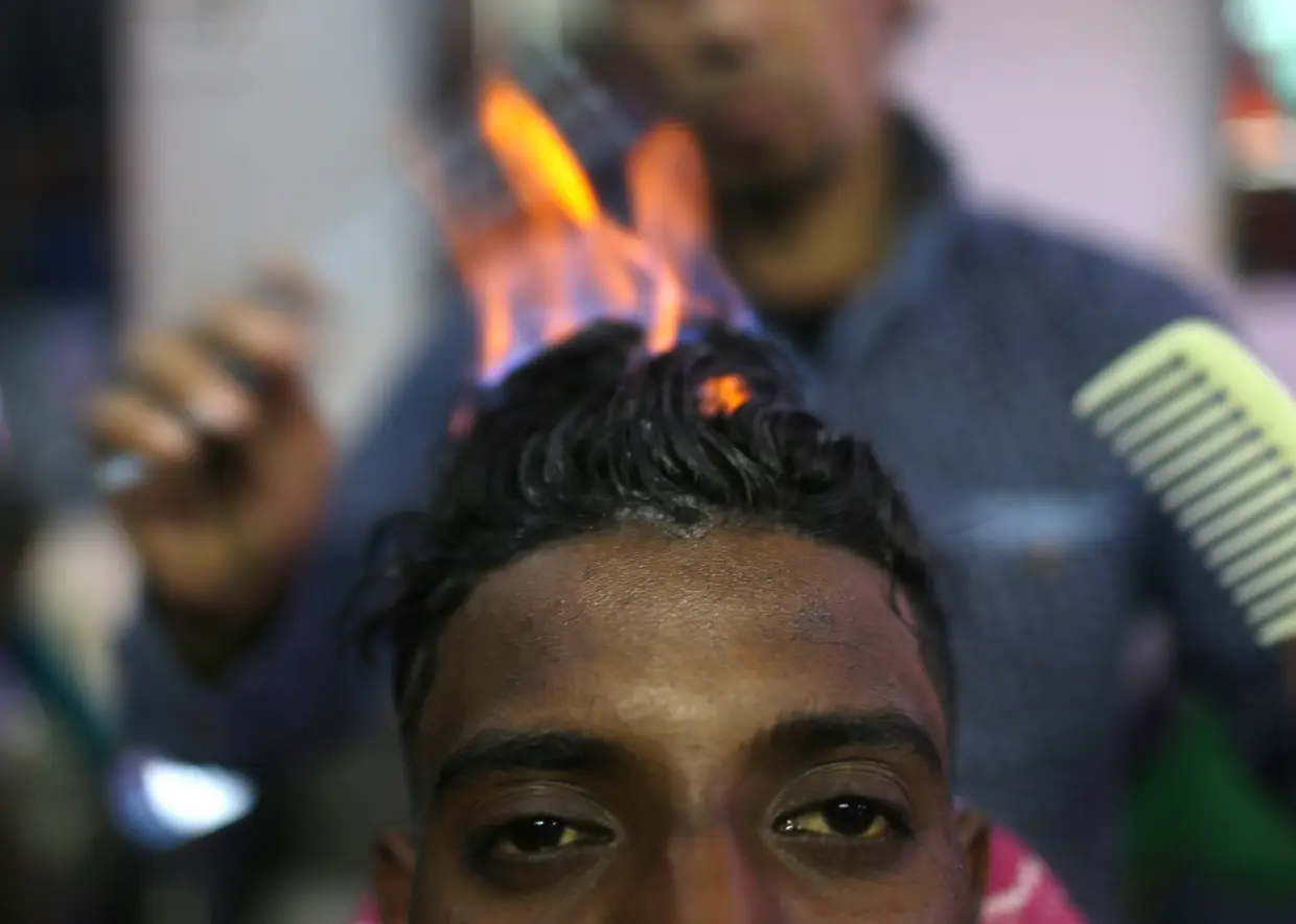Barbeiro palestiniano usa fogo para fortalecer e e modelar o cabelo de um cliente no seu estabelecimento em Rafah, a sul da Faixa de Gaza.