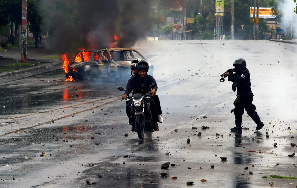 Um polícia atira sobre dois manifestantes durante um protesto contra o presidente Daniel Ortega, em Nicarágua.