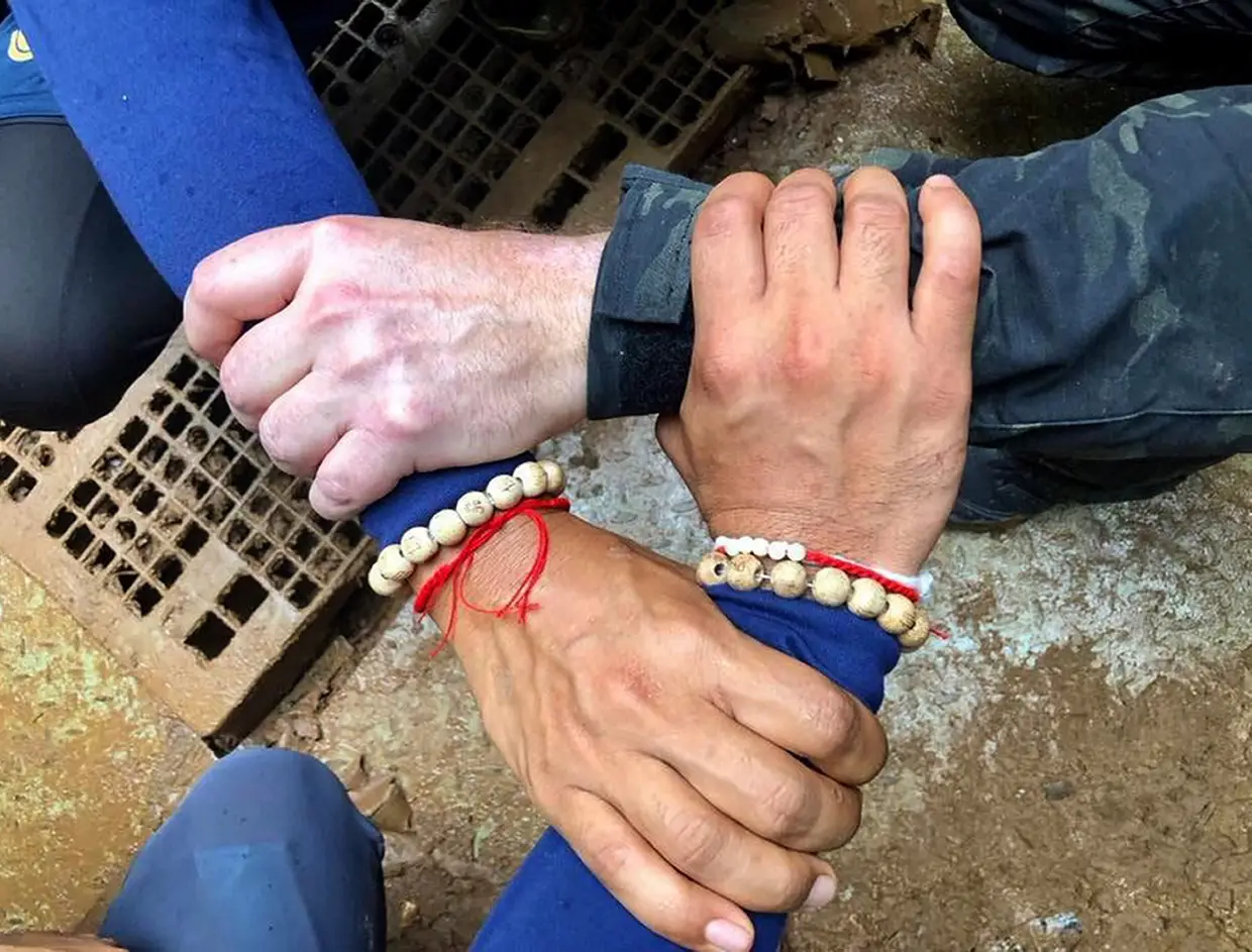 Uma fotografia de militares tailandeses com as mãos entrelaçadas, com a mensagem: "Nós - Thai [Marinha} - e as equipas internacionais a unir forças para trazer os "jovens javalis" para casa".