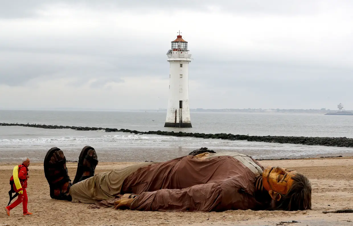 Um nadador-salvador passa junto a uma marioneta gigante numa praia em New Brighton, Reino Unido