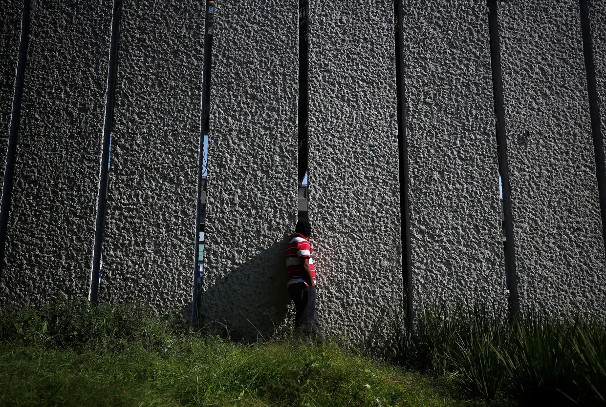 Um migrante que faz parte da caravana que caminha em direção aos EUA espreita através da parede para a Cidade do México.
