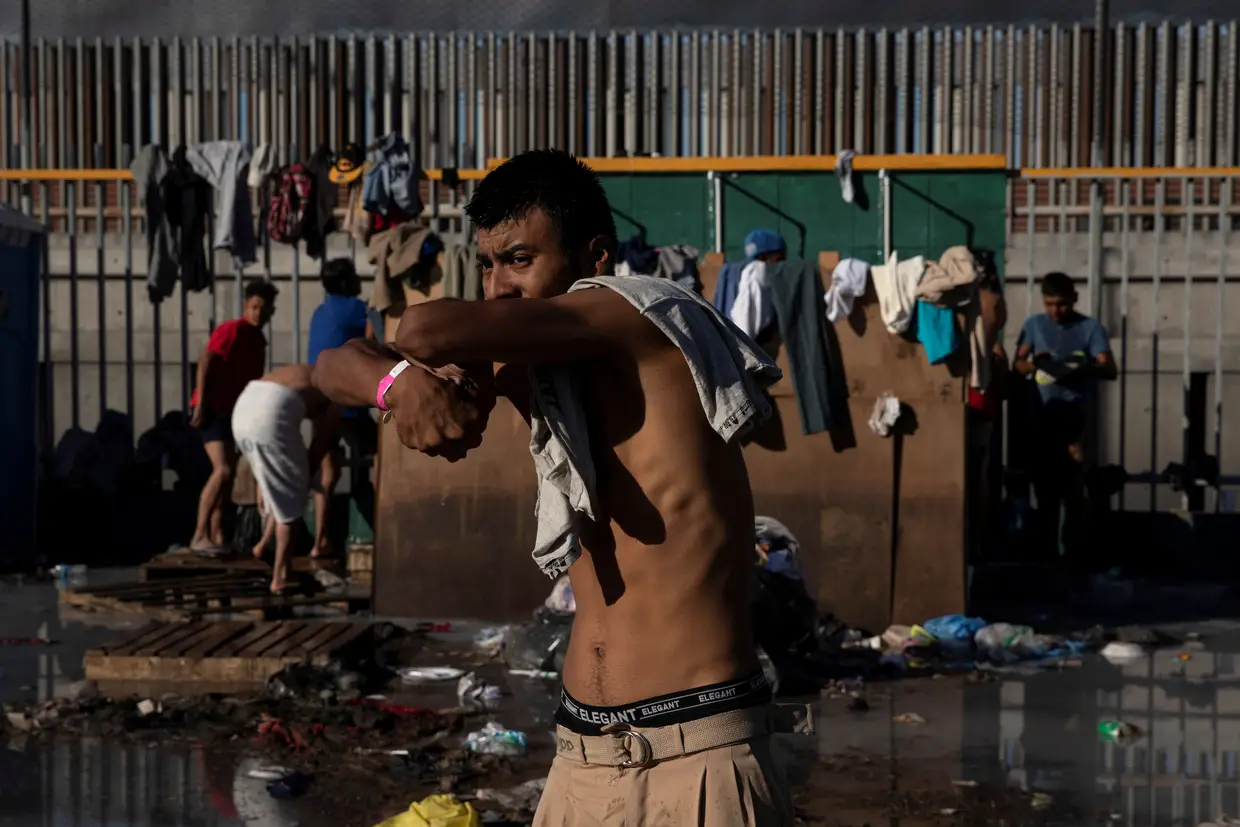Um migrante da caravana da América Central espreme água das roupas lavadas, num refúgio temporário em Tijuana.