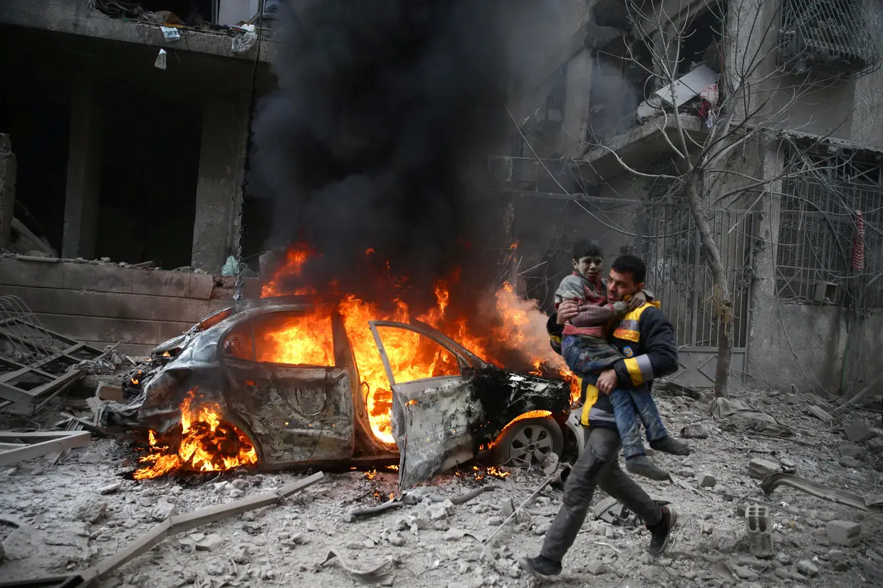 Um membro da Defesa Civil Síria carrega uma criança ferida na cidade de Hamoria, no leste de Ghouta, em Damasco.