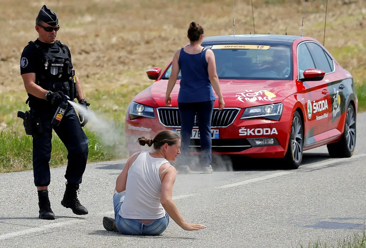 Um polícia atira gás pimenta a uma manifestante durante a Volta à França em bicicleta.