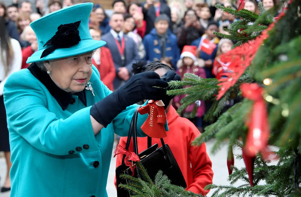 A Rainha Isabel II e uma criança penduram um enfeite num árvore de natal durante uma visita à instituição de caridade infantil Coram em Londres, Reino Unido