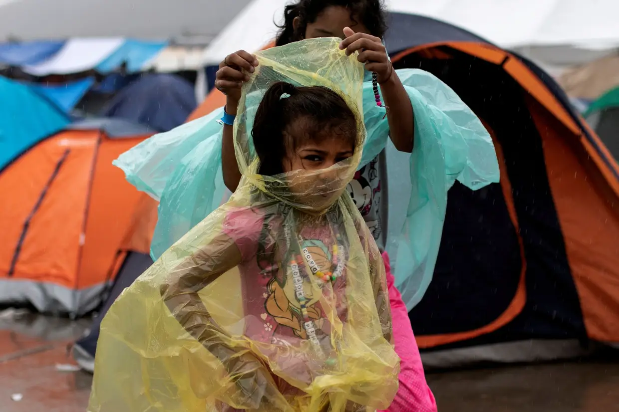 Uma rapariga, que faz parte de uma caravana proveniente da América Central, usa uma capa de chuva no abrigo temporário em Tijuana, no México