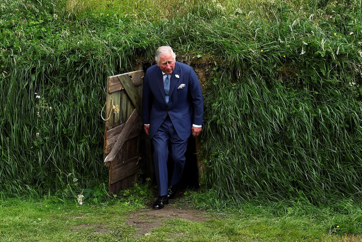 O príncipe Carlos emerge da recriação de uma cabana de barro da época da grande fome de 1845–1849 na Irlanda, no campus da University College Cork.