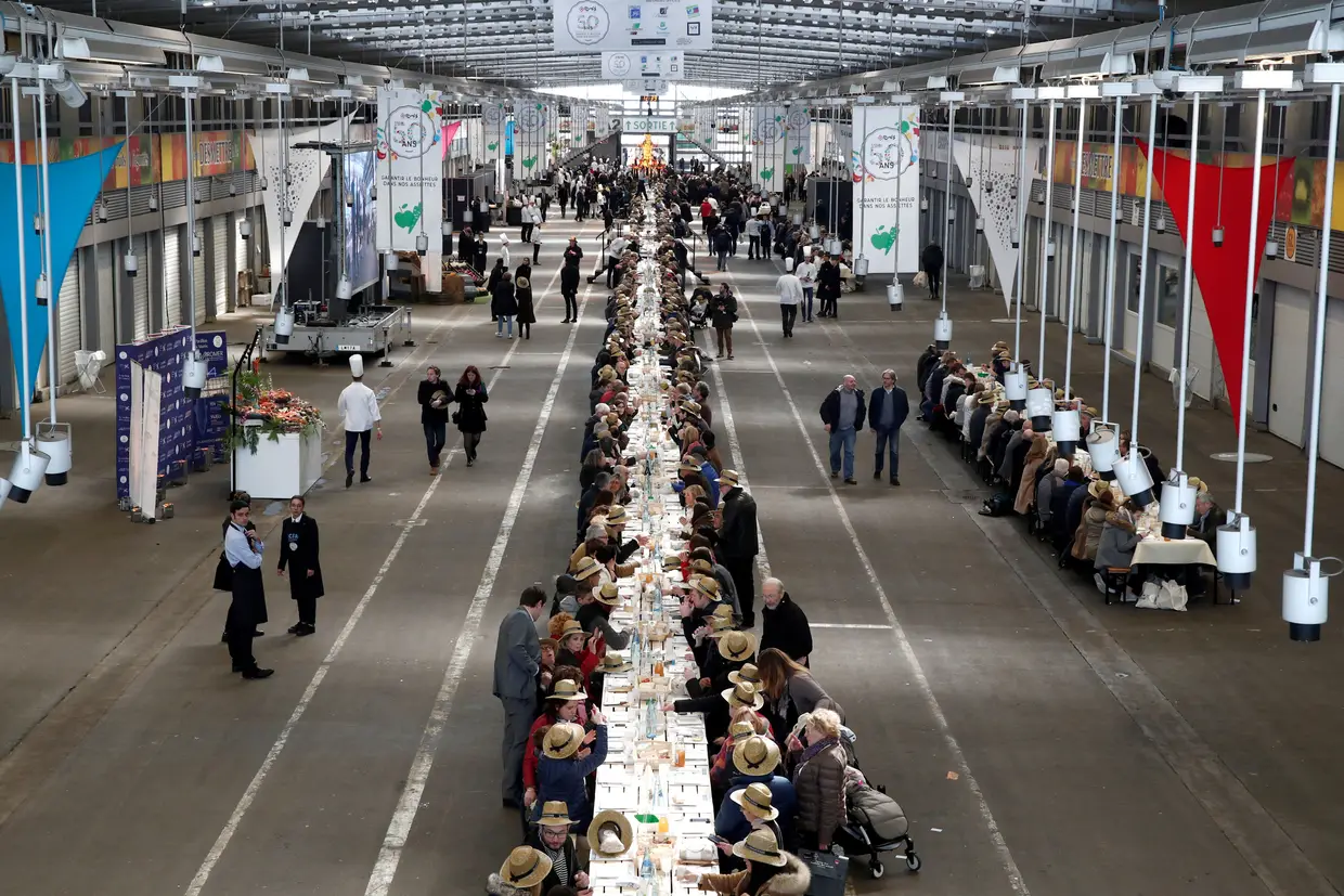 Participantes sentam-se numa mesa de mais 400 metros, num almoço no Mercado Internacional de Comida de Rungis, perto de Paris, em França.