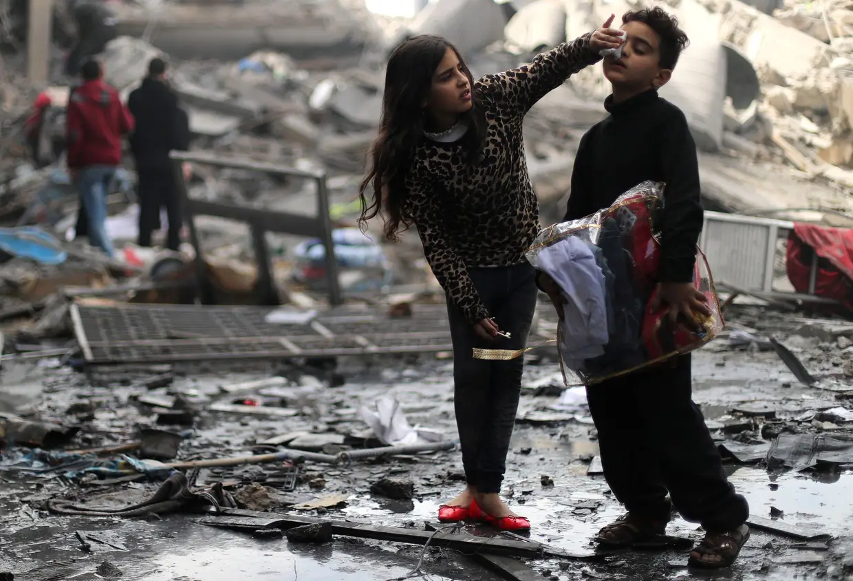 Uma criança palestiniana limpa o rosto do irmão, junto aos destroços da sua casa, destruída por um míssil israelita.