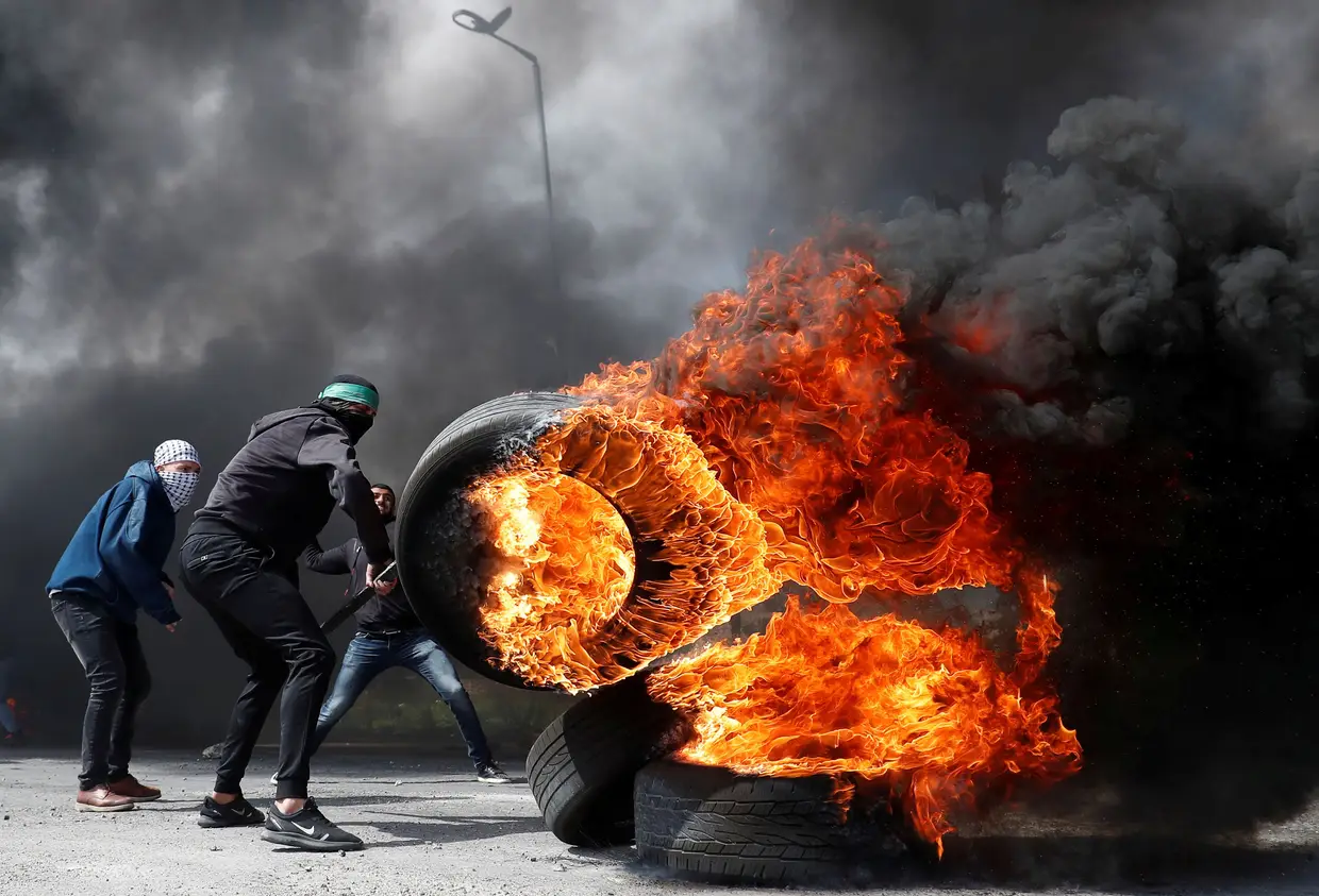 Um manifestante palestiniano move um pneu em chamas durante confrontos com tropas israelitas, na Cisjordânia.
