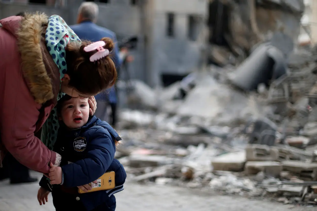 Uma palestiniana conforta o filho junto aos destroços de sua casa, destruída por bombardeamentos de Israel, em Gaza.