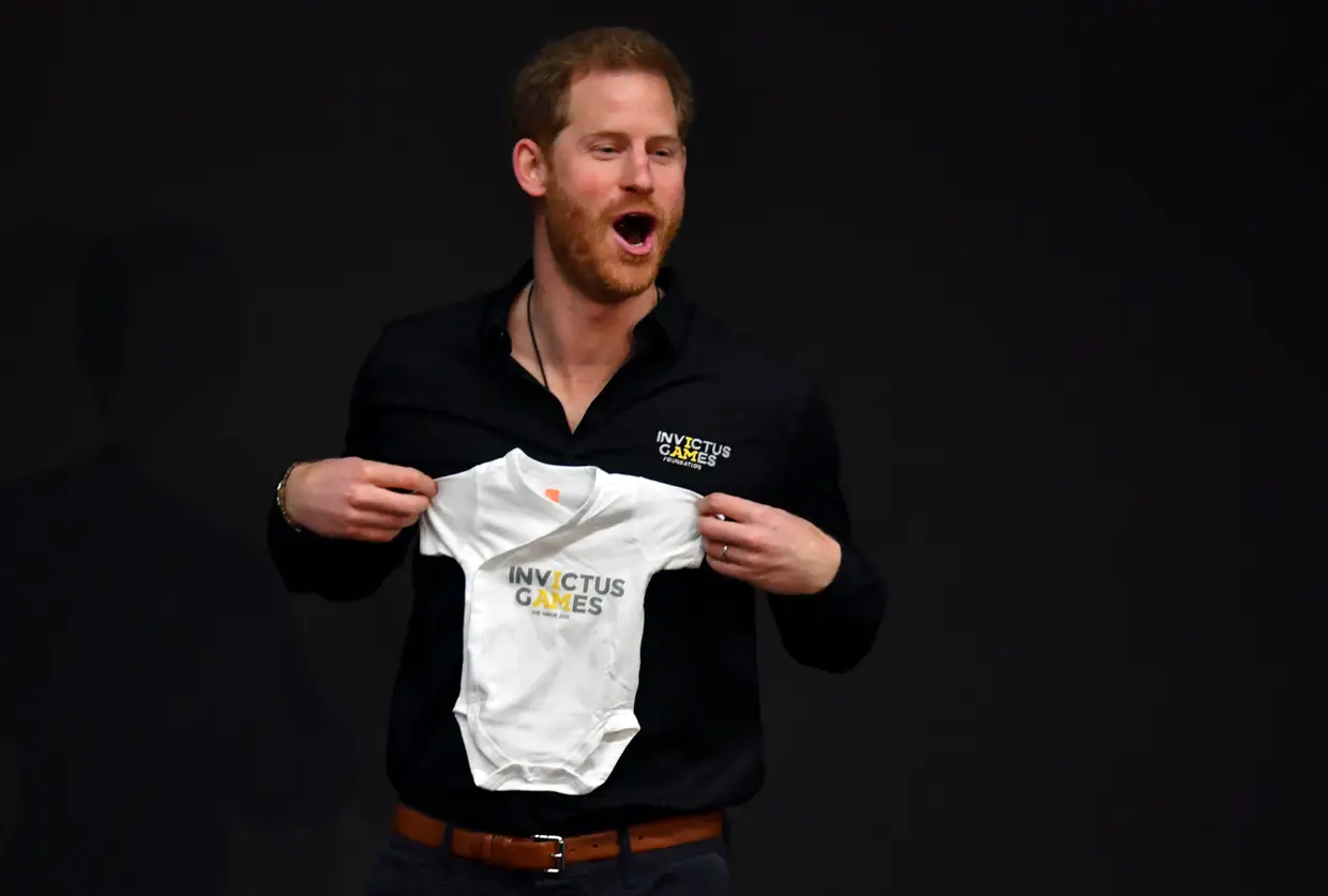 O príncipe Harry segura roupa de bebé durante a inauguração oficial dos "Invictus Game" em Haia, na Holanda.