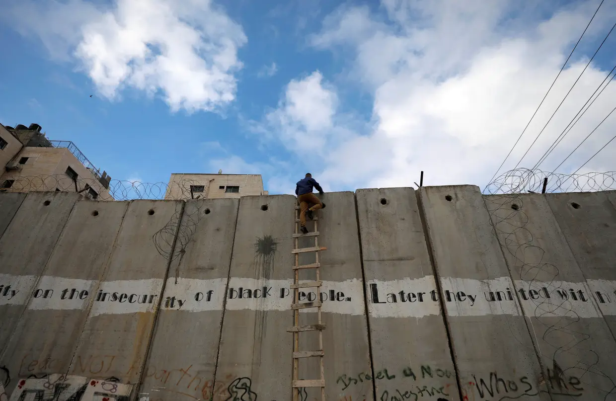 Um palestino escala o Muro da Cisjordânia para ir assistir às primeiras orações de sexta-feira, na mesquita de Al-Aqsa, durante o mês do Ramadão.
