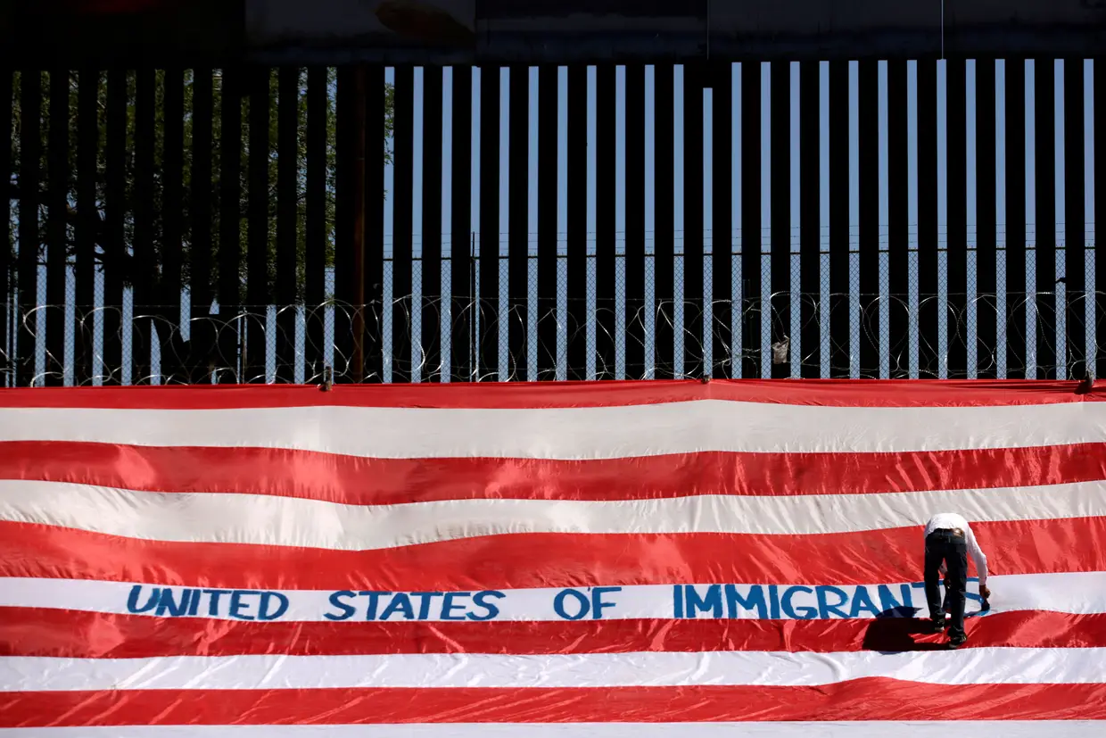 Um manifestante escreve numa bandeira dos Estados Unidos num protesto intitulado "United States of Immigrants" (Estados Unidos dos Imigrantes) junto à fronteira de El Paso, Texas.
