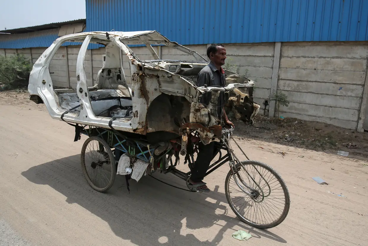 Um homem carrega num triciclo um carro desmontado para sucata, em Ahmedabad, Índia.
