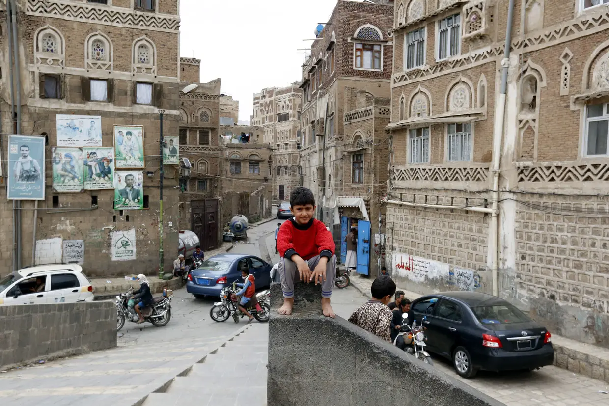 Uma criança sentada em frente a edifícios históricos, em Sanaa, Iémen.