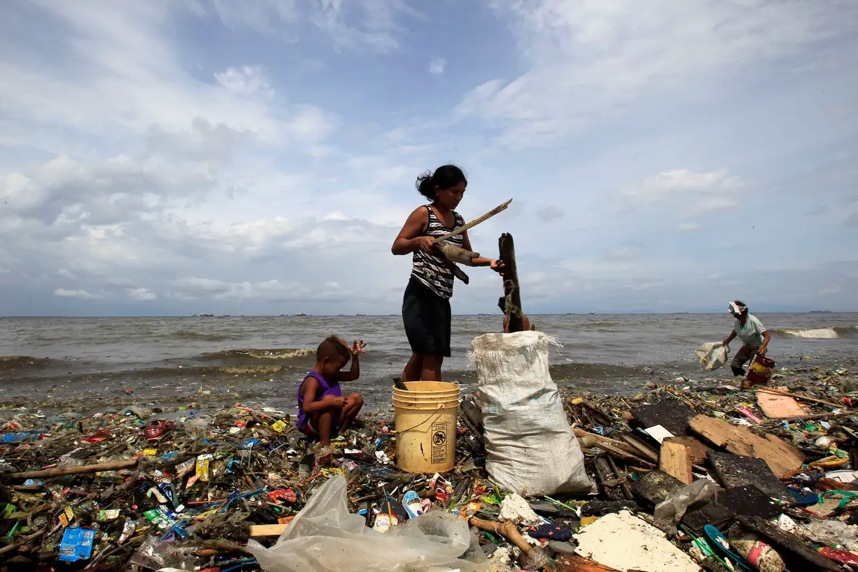 Mãe e filho procuram plástico para vender que dá à costa em Manila, Filipinas