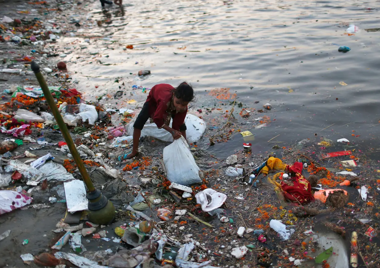 Menina recolhe as oferendas lançadas ao rio Yamuna em Nova Deli, Índia