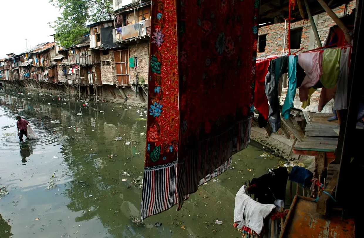 Homem recolhe lixo de plástico para reciclar num rio poluído que atravessa um bairro de lata em Jacarta, Indonésia