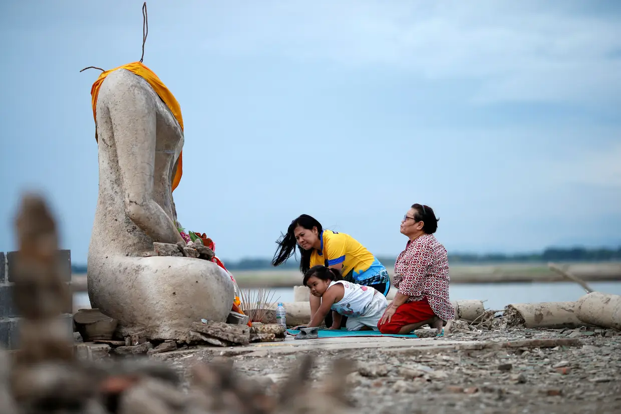 Uma família reza junto a templo budista, em Lopburi, Tailândia, que estave submerso numa barragem. O templo foi revelado depois de um período de seca que deixou os níveis de água a registar mínimos históricos.
