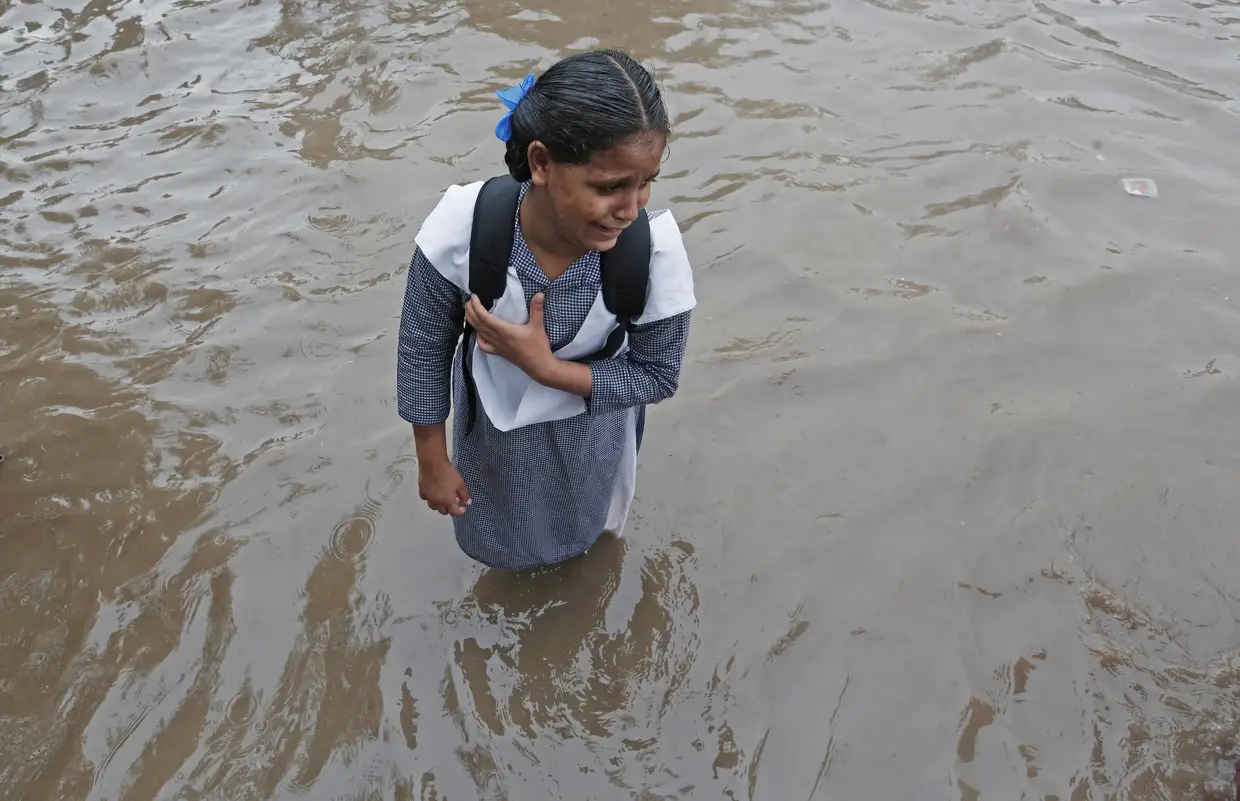 Uma criança chora ao atravessar uma rua inundada pelas cheias em Nova Déli, Índia.