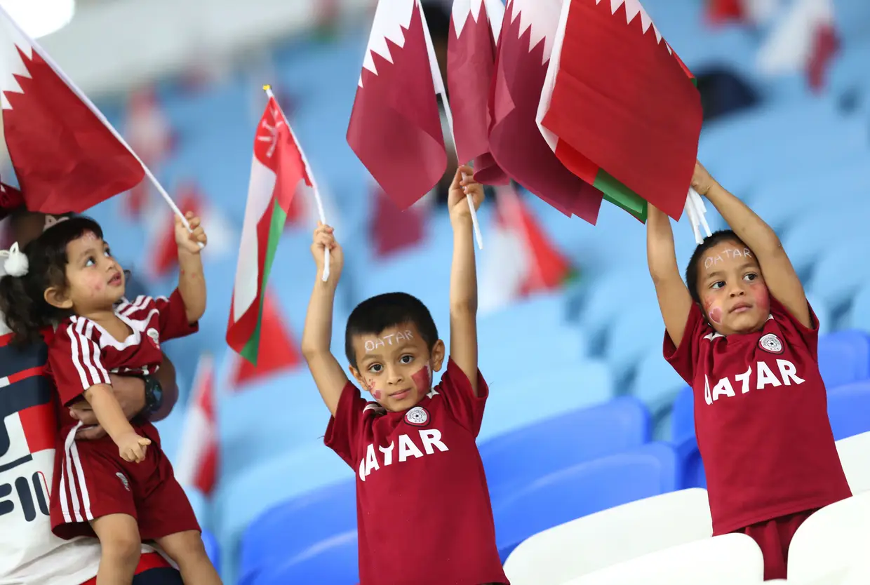 Crianças com as caras pintadas seguram bandeiras de Omã e do Qatar durante um jogo de qualificação para o Mundial de futebol de 2022, Qatar.