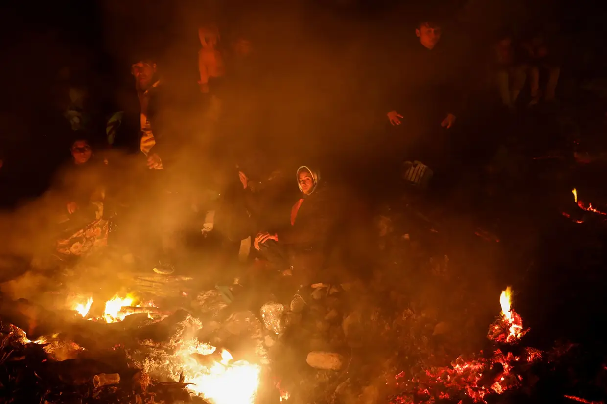Migrantes provenientes do Afeganistão aquecem-se junto a uma fogueira numa praia em Lesbos, Grécia.