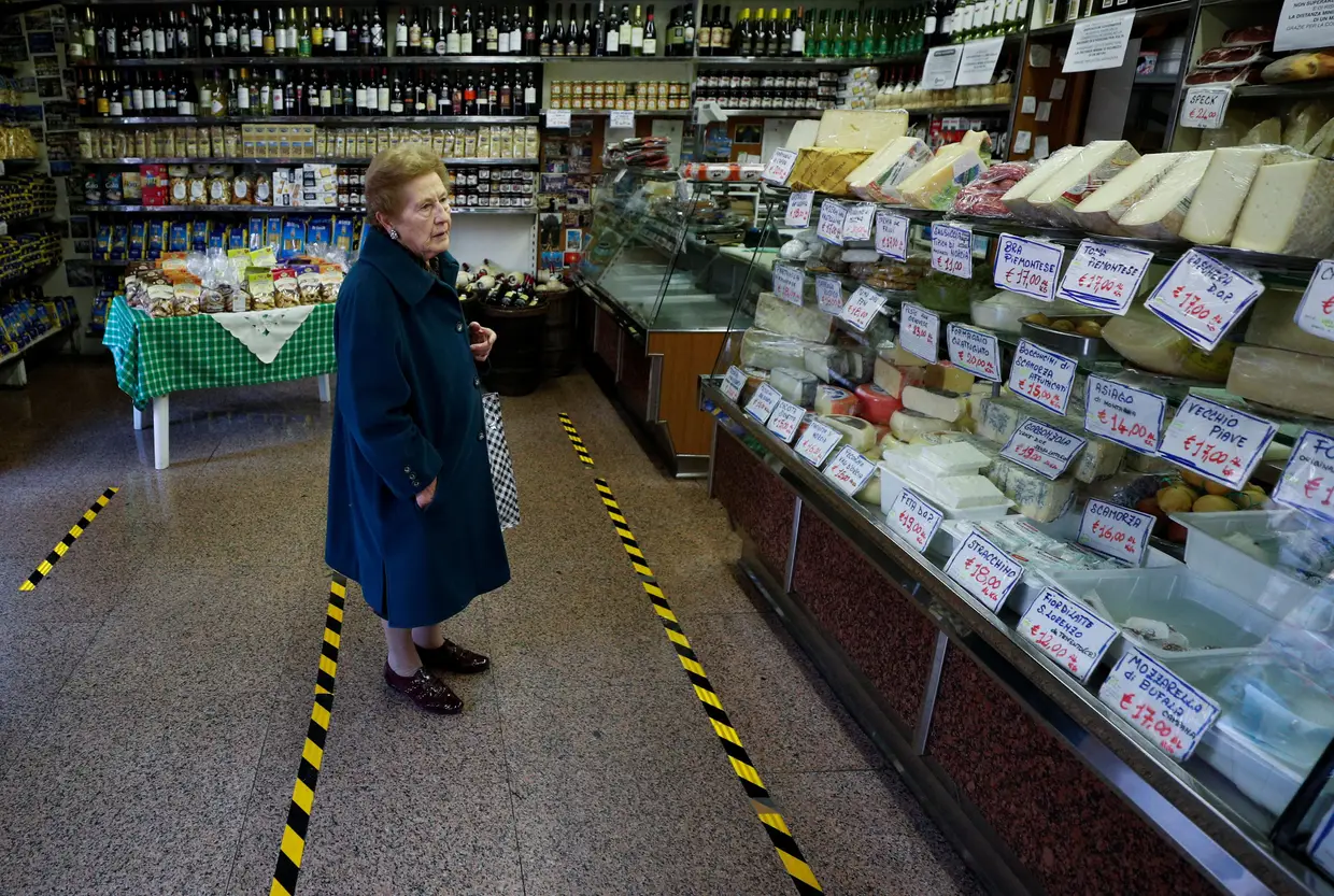 Uma italiana aguarda pela vez de ser atentida numa mercearia, cumprindo a distância imposta dos alimentos em exposição.