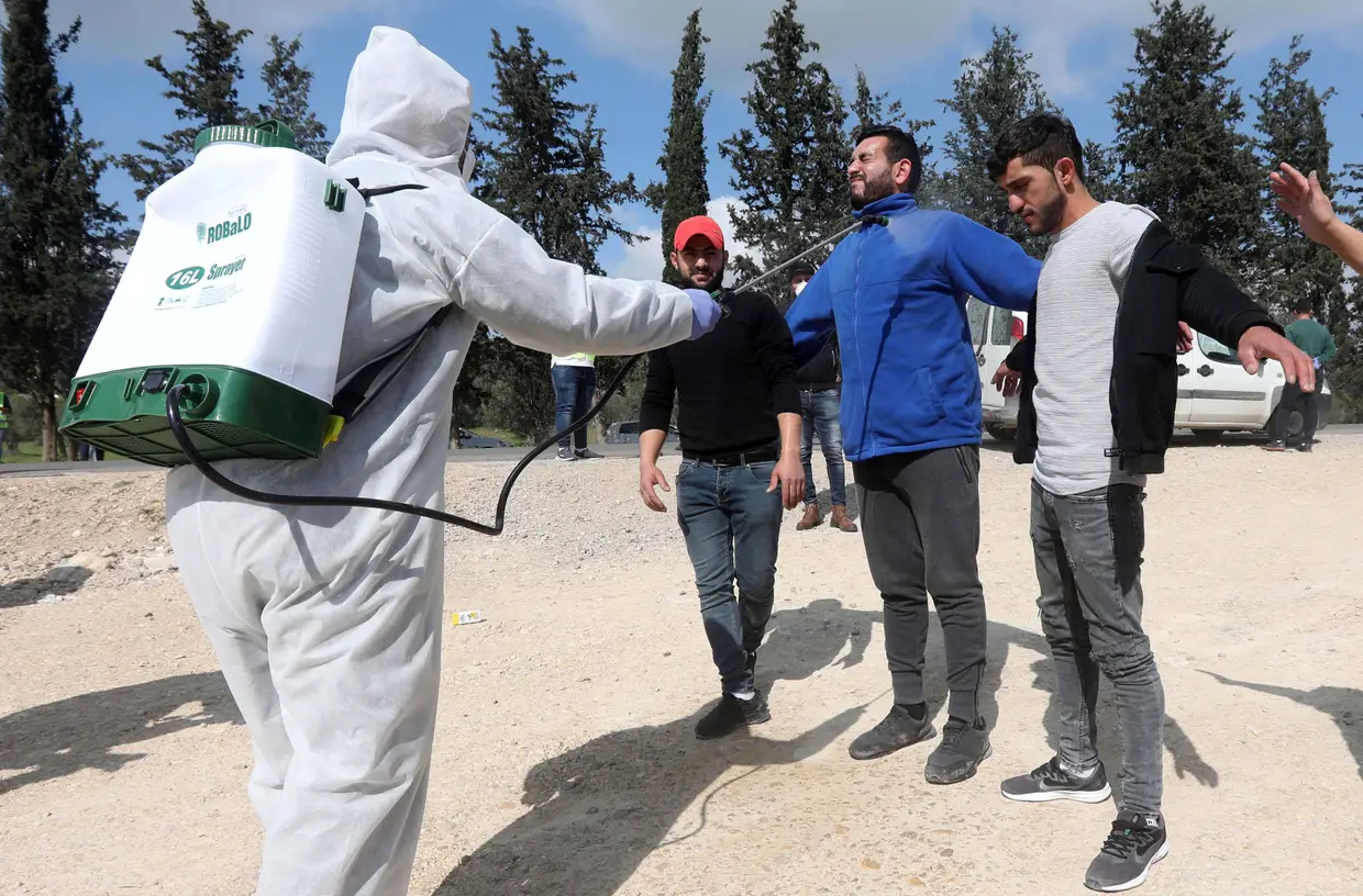 Um funcionário do Ministério da Saúde palestiniano borrifa desinfetante em trabalhadores que regressam de Israel, no posto de controlo de Tarqumiyah, em Hebrom, cidade palestiniana da Cisjordânia.