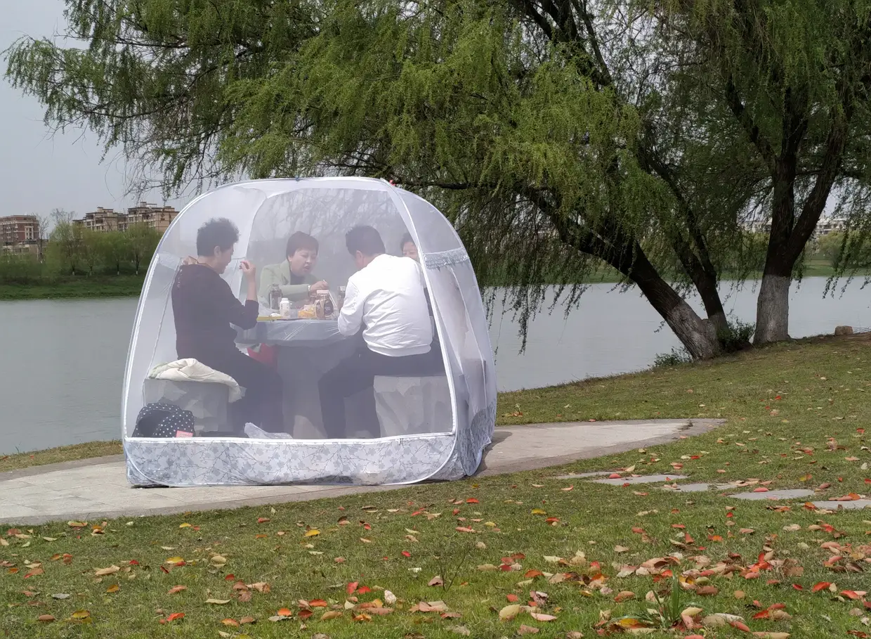 Pessoas desfrutam de uma refeição dentro de uma tenda num parque na China para prevenir a propagação da Covid-19.