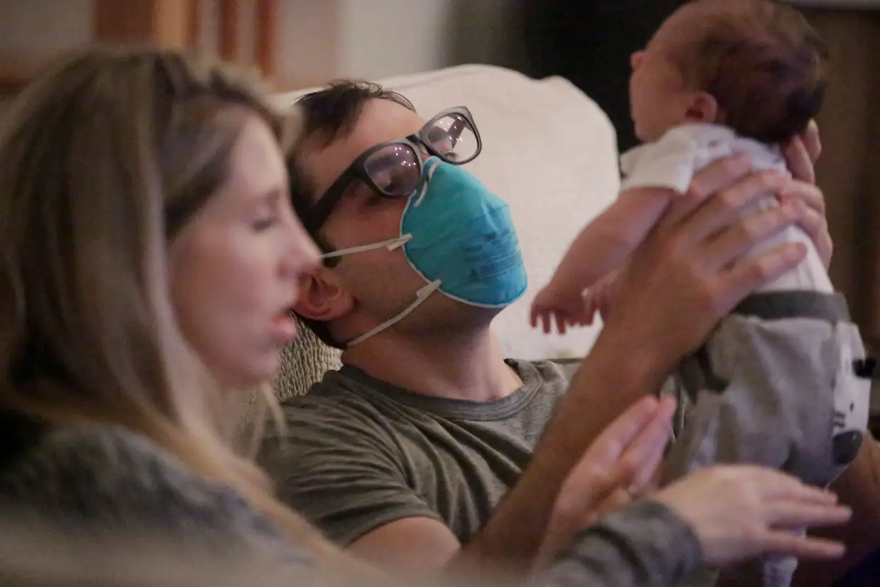 Um profissional de saúde utiliza uma máscara de proteção enquanto pega no seu filho depois de ter terminado um turno de trabalho, em Nova Orleães, Luisiana, Estados Unidos.