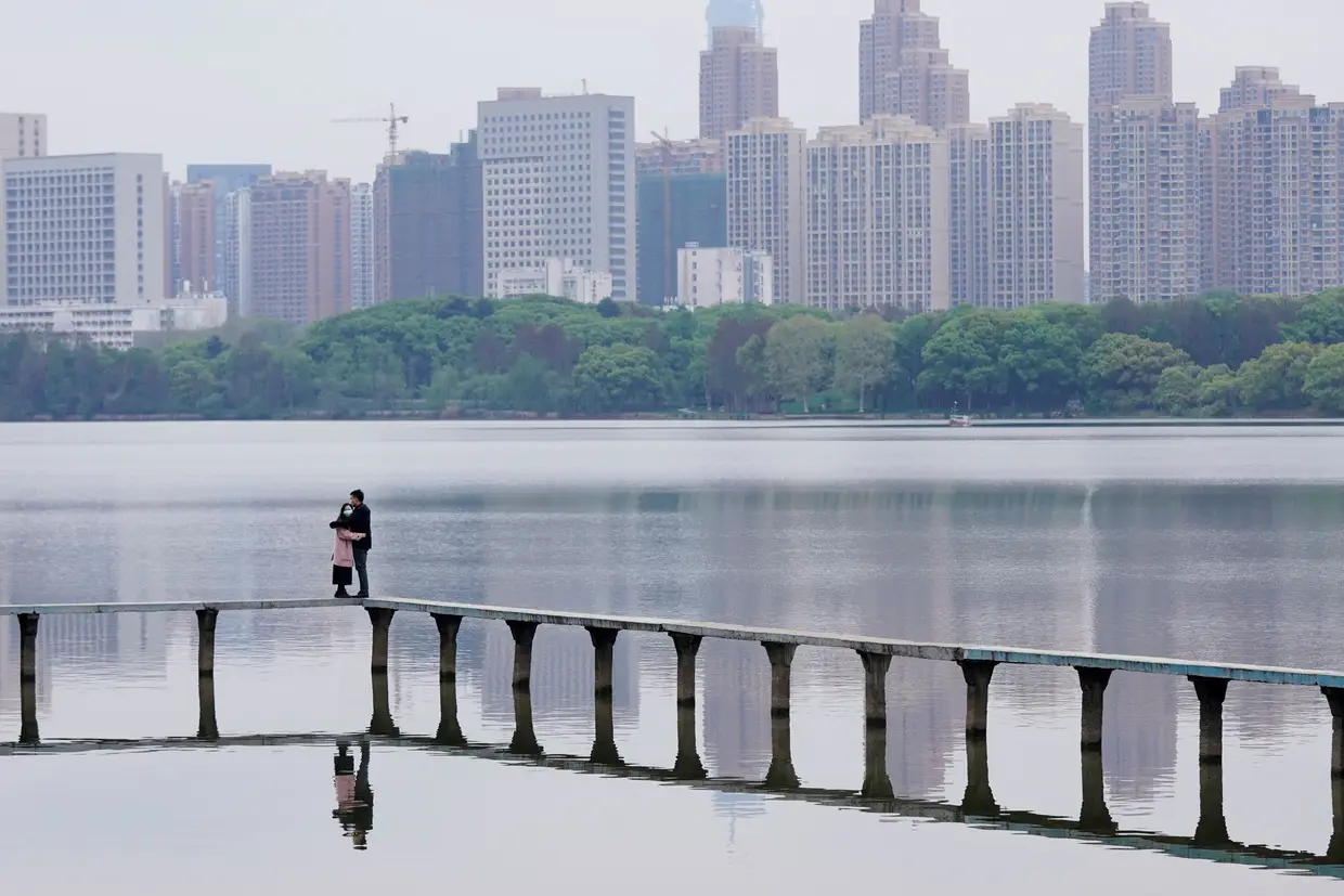 Duas pessoas abraçam-se num lago em Wuhan, na China, enquanto utilizam máscaras de proteção.