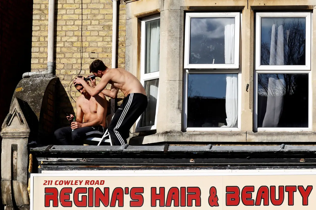 Um jovem corta o cabelo de outro em cima de um cabeleireiro fechado, em Oxford, Inglaterra.