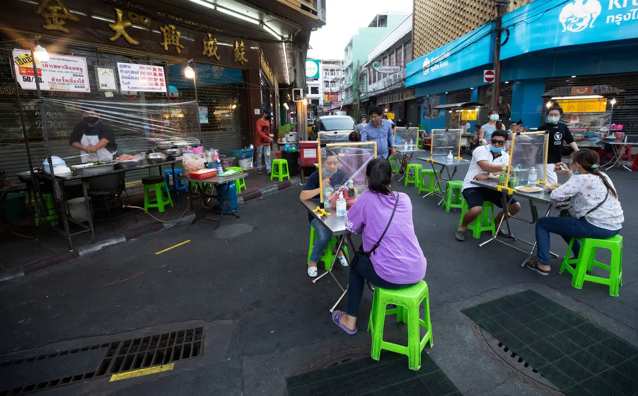 Clientes de um restaurante em Bangkok, na Tailândia, a almoçar com divisórias de proteção de plástico.
