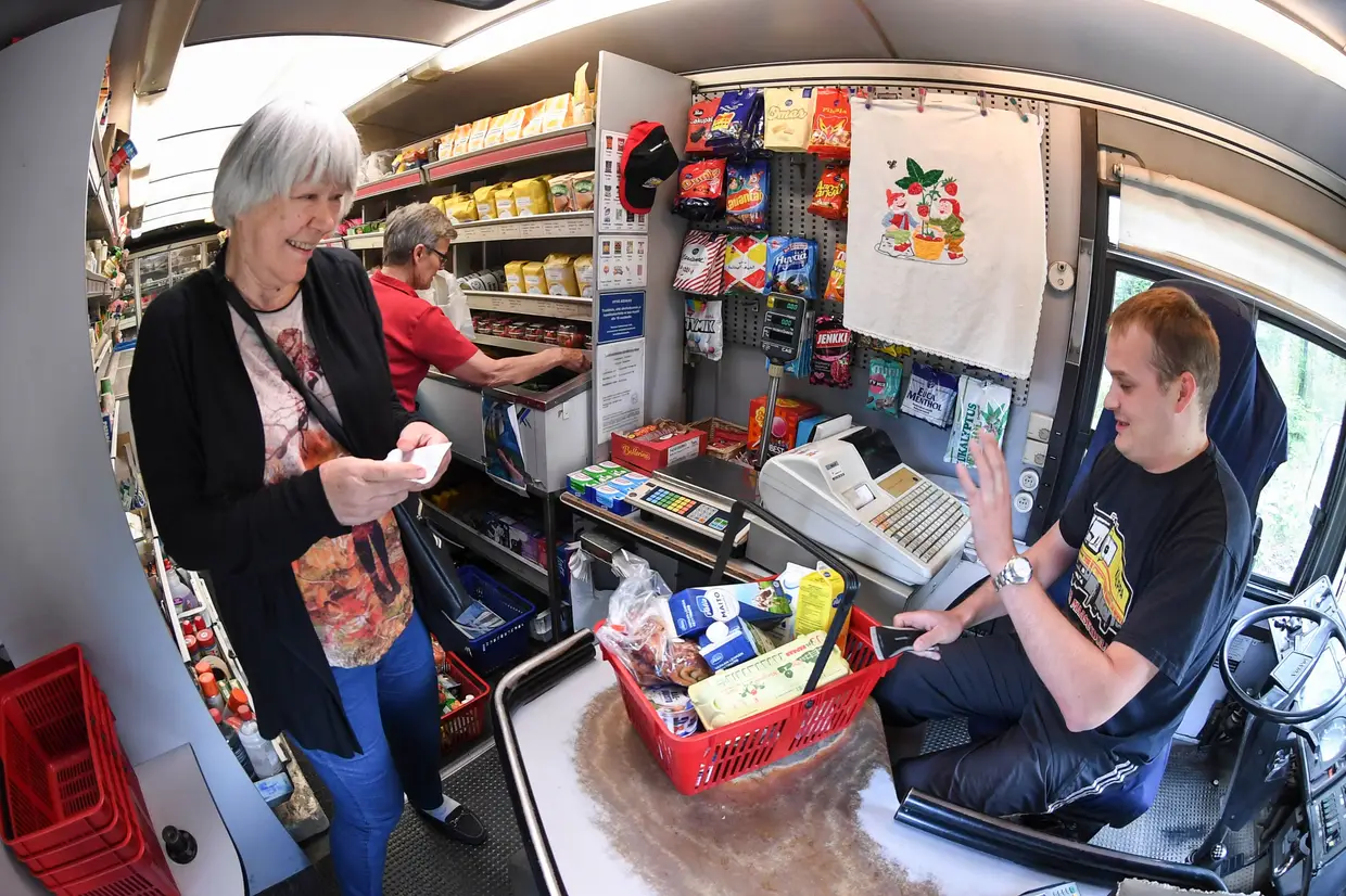 Clientes fazem compras num supermercado móvel dentro de um autocarro em Punkaharju, na Finlândia. Antigamente, era comum existirem supermercados móveis que serviam os clientes que viviam no Interior do país, mas hoje em dia só restam seis veículos deste género.