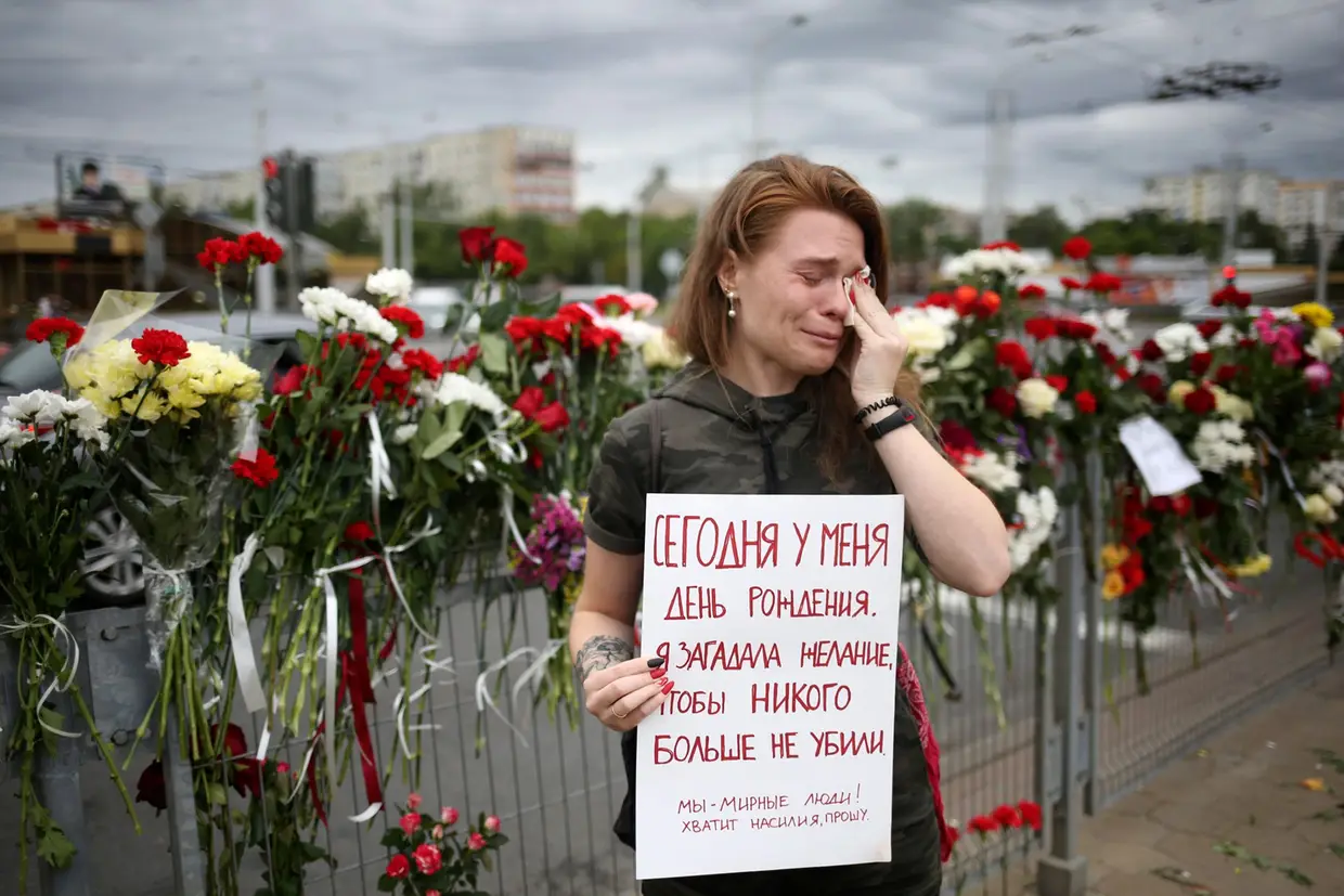 Uma mulher segura um cartaz no local onde morreu um manifestante em Minsk, na Bielorrússia. No cartaz pode ler-se "É o meu aniversário. Peço para que mais ninguém seja morto. Somos um povo pacífico. Chega de violência, por favor".