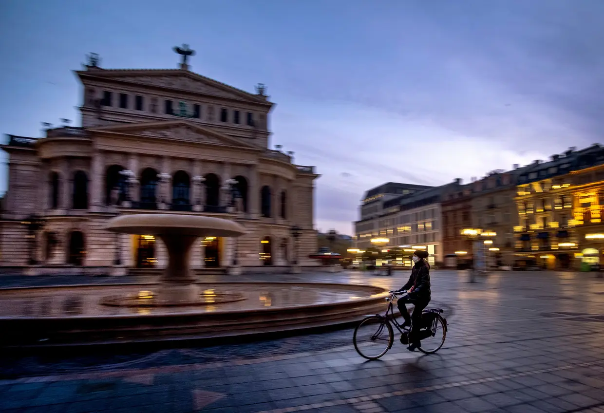 Uma mulher atravessa de bicicleta uma praça vazia em Frankfurt, na Alemanha.
