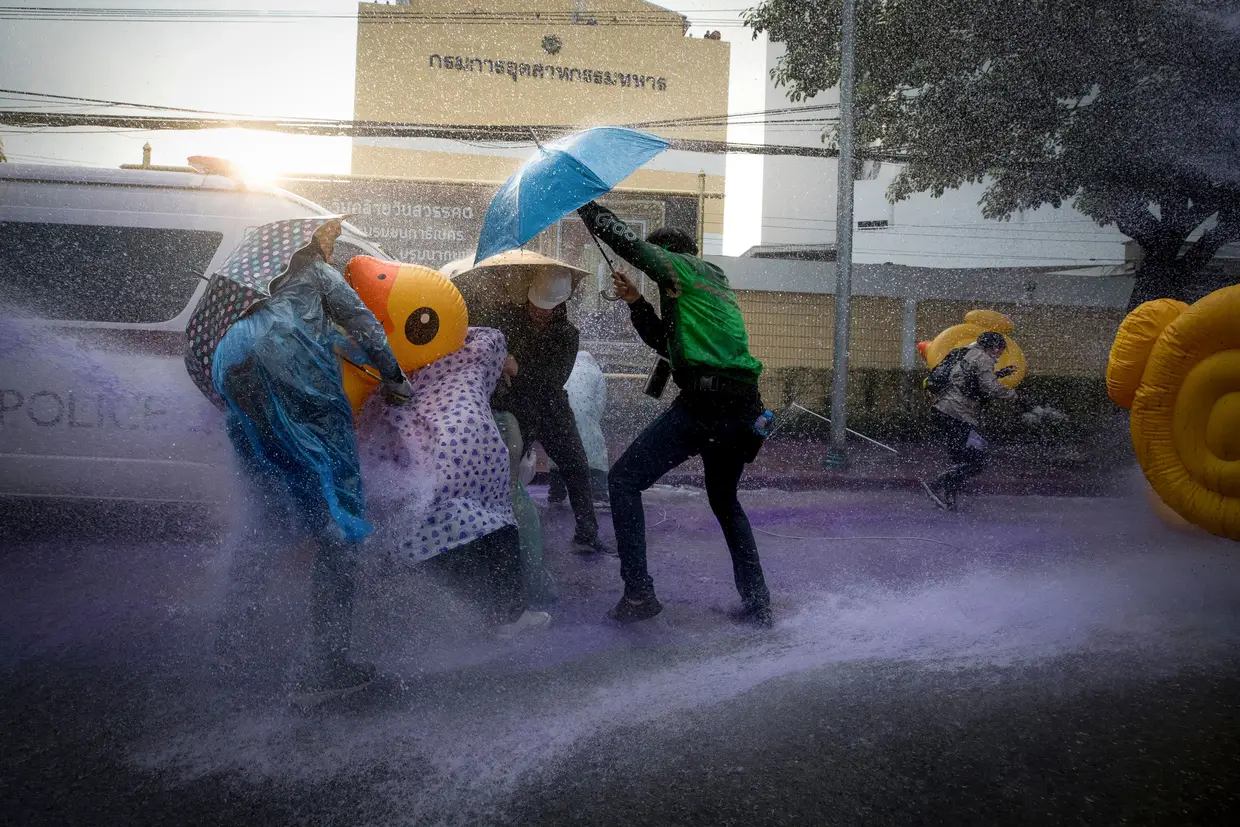 Manifestantes pró-democracia protegem-se, enquanto as autoridades lançam canhões de água durante um protesto contra o governo, perto do Parlamento, em Banguecoque, na Tailândia.