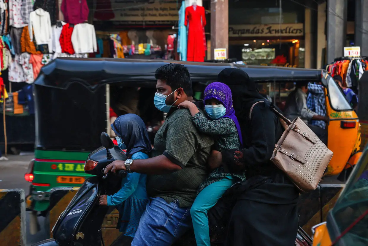 Uma família indiana a usar máscara de proteção contra a covid-19 atravessa uma rua em Hyderabad, na India, de mota.