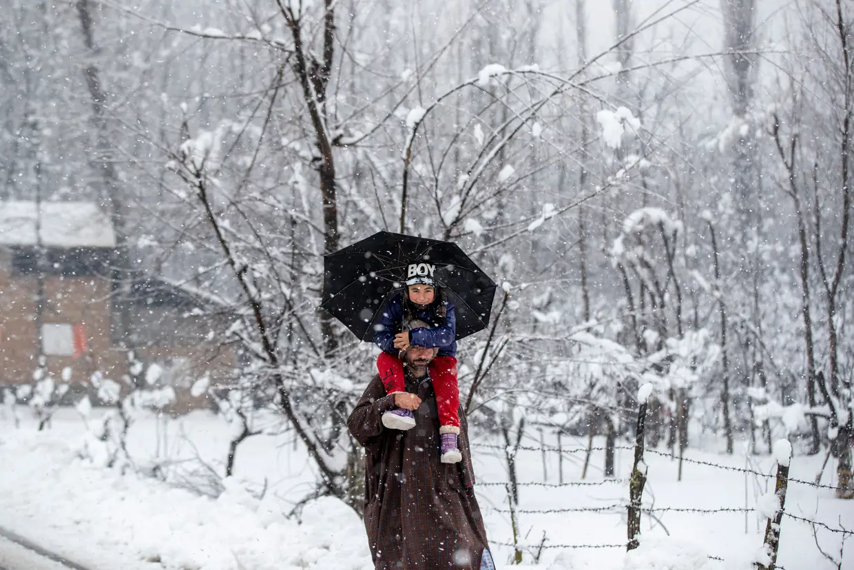 Um homem com o filho nos ombros enquanto neva na cidade de Srinagar, na região de Caxemira controlada pela Índia.