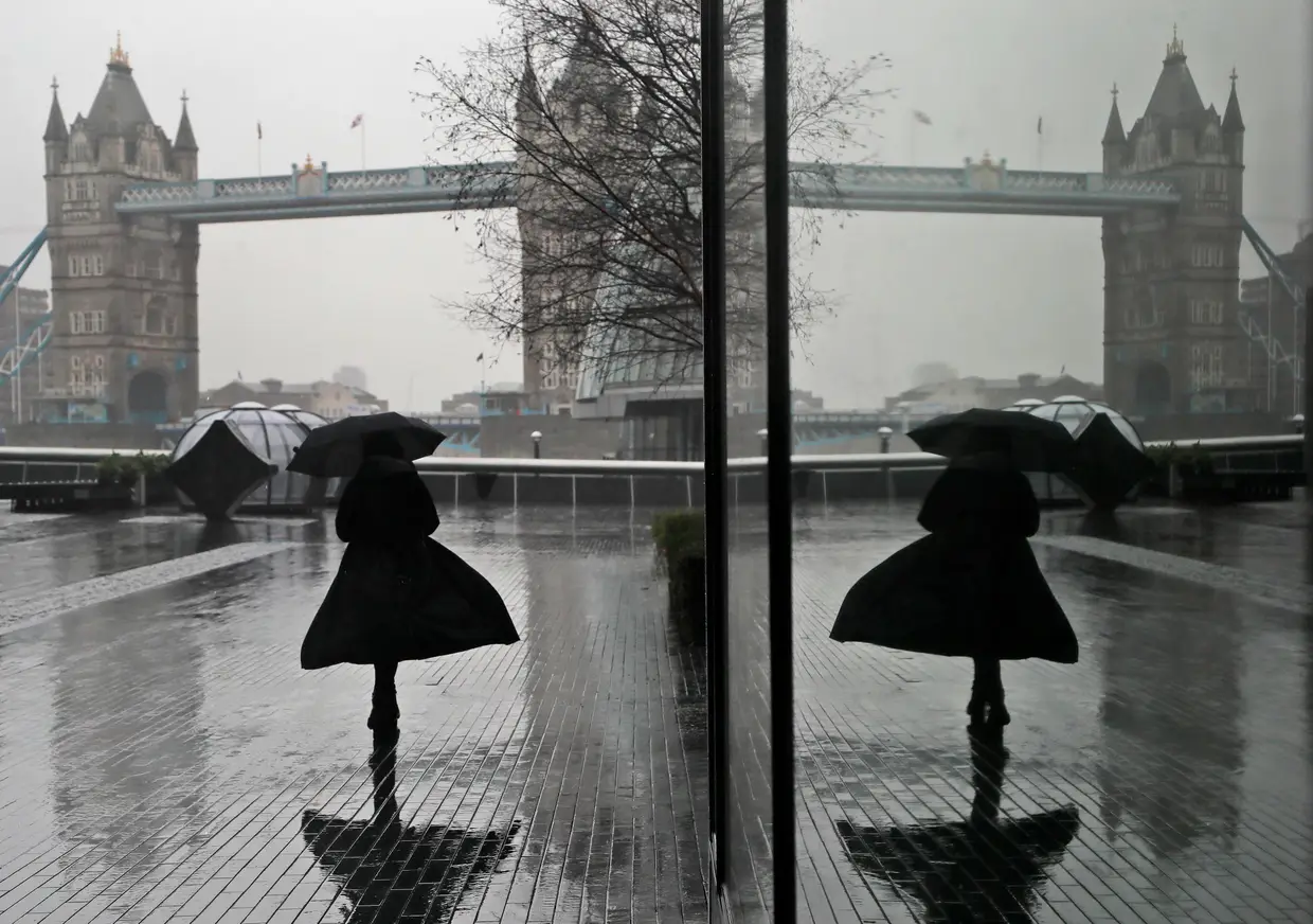 Uma mulher refletida numa janela enquanto enfrenta o vento e a chuva em Londres, durante o terceiro confinamento no Reino Unido para conter a pandemia.