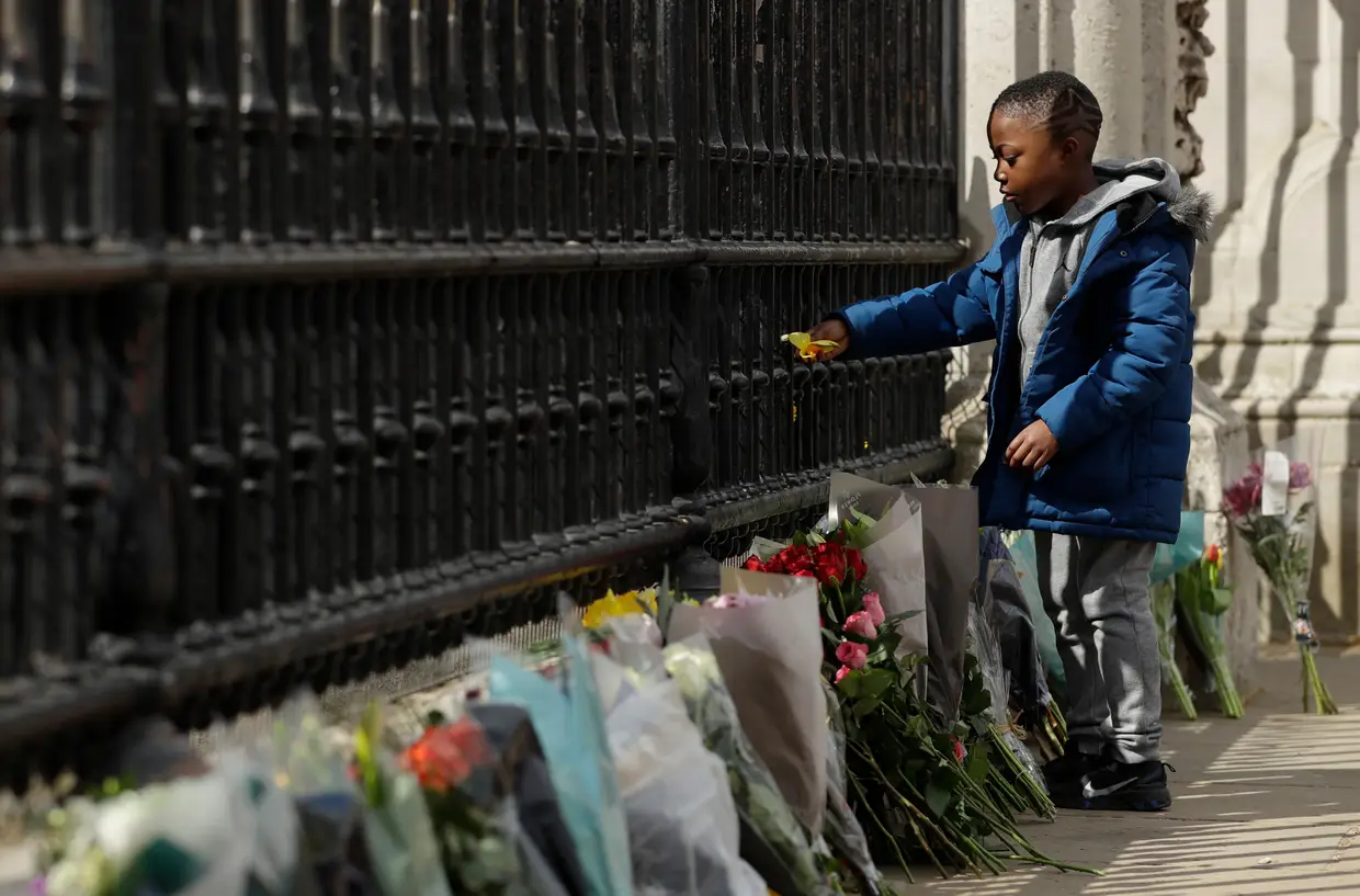 Criança coloca uma flor no portão do Palácio de Buckingham, em homenagem ao Príncipe Filipe, marido da Rainha Isabel II, que morreu aos 99 anos.