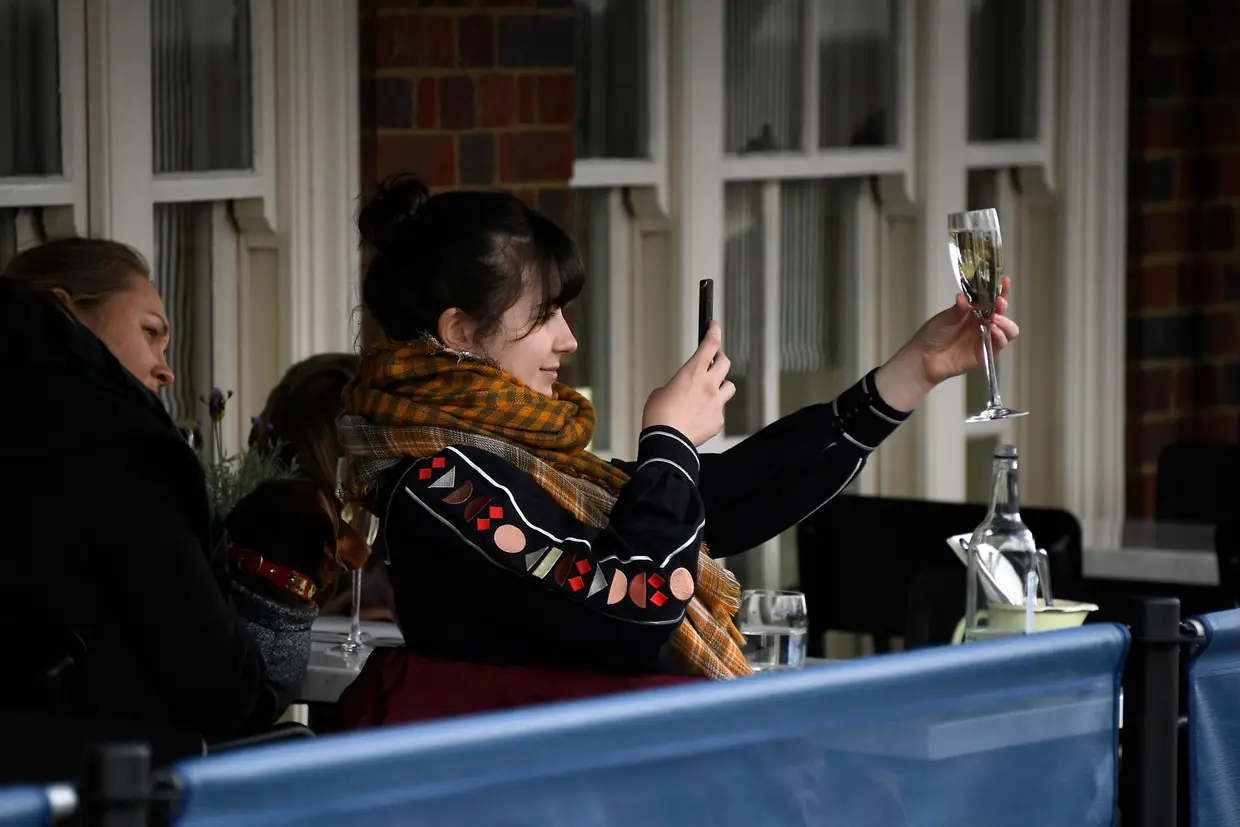 Mulher tira fotografia ao copo de vinho, na varanda de um pub em Londres, numa altura em que o Reino Unido alivia as medidas de restrição devido à covid-19.