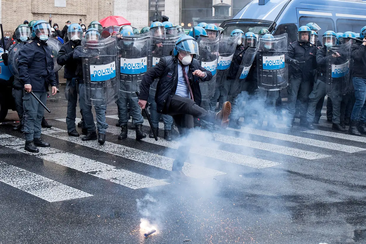 Um polícia pontapeia um explosivo durante uma manifestação contra as medidas de restrições impostas aos restaurantes e aos pequenos comércios devido à covid-19, em Roma, Itália.