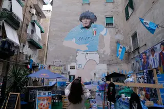 Turista fotografa o mural de Diego Maradona na chamada "Praça de Maradona" no bairro Quartieri Spagnoli de Nápoles. O jogador argentino que morreu aos 60 anos, a 25 de novembro de 2020, continua a ser idolatrado na cidade italiana. A image do jogador está por toda a parte, no primeiro aniversário da sua morte. Considerado um dos melhores futebolistas da história, Maradona foi campeão do mundo em 1986, vencedor de dois campeonatos em Itália e de uma Taça UEFA pelo Nápoles.