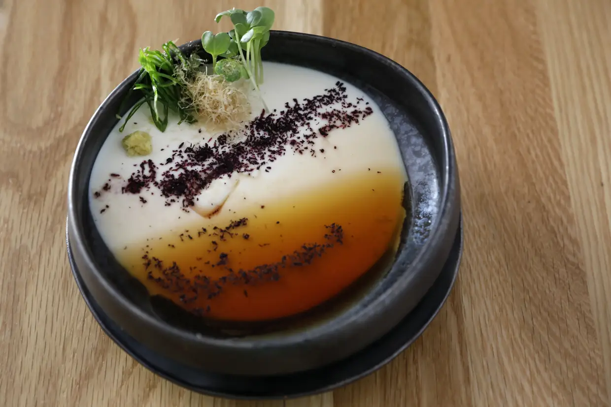 Nas entradas frias, destaca-se o House Made Tofu, com dashi de soja vegan, gengibre, cebolo, bonito seco, microgreens e sal yukari